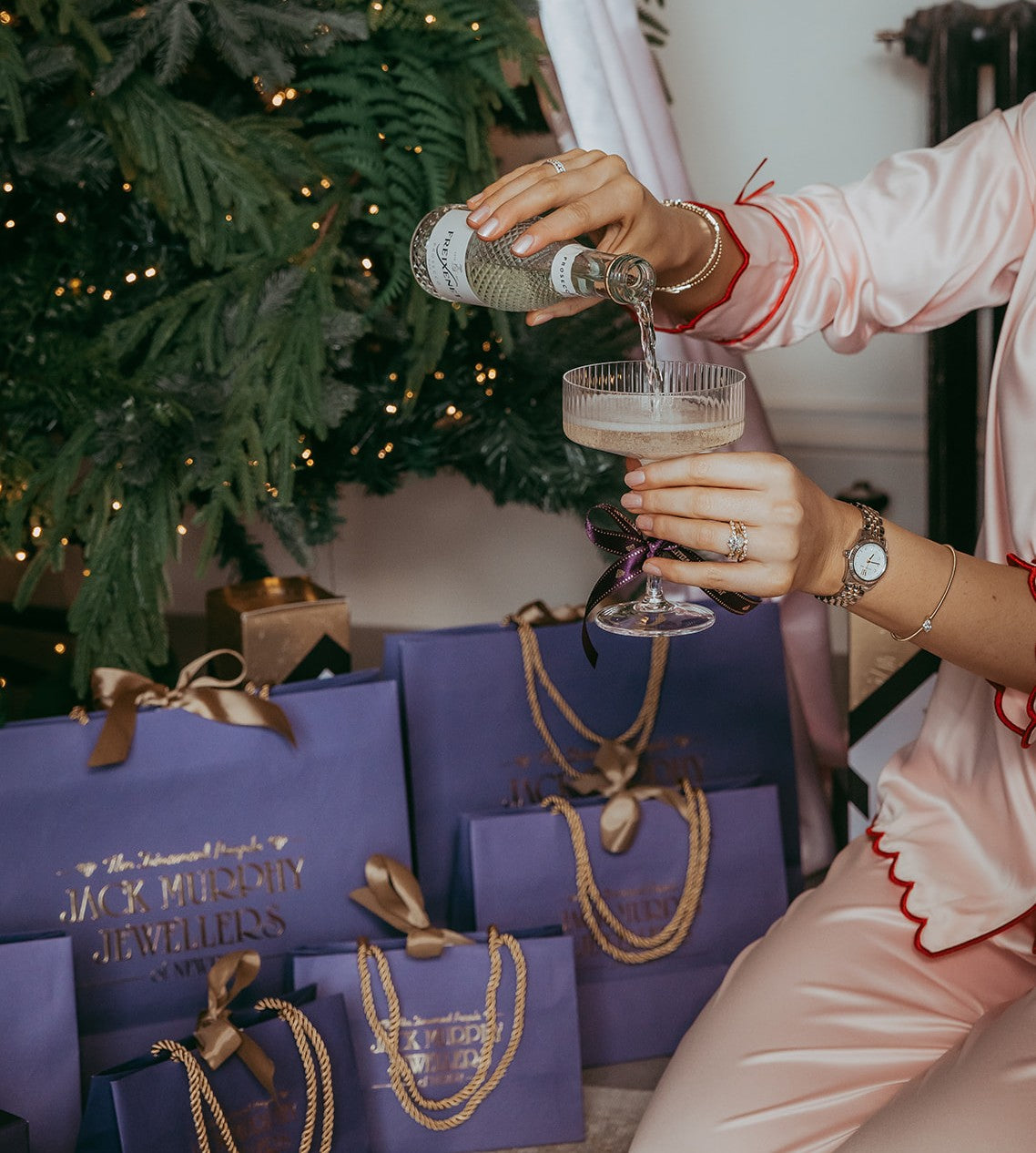 Person pouring a drink into a glass with Christmas tree and presents in the background